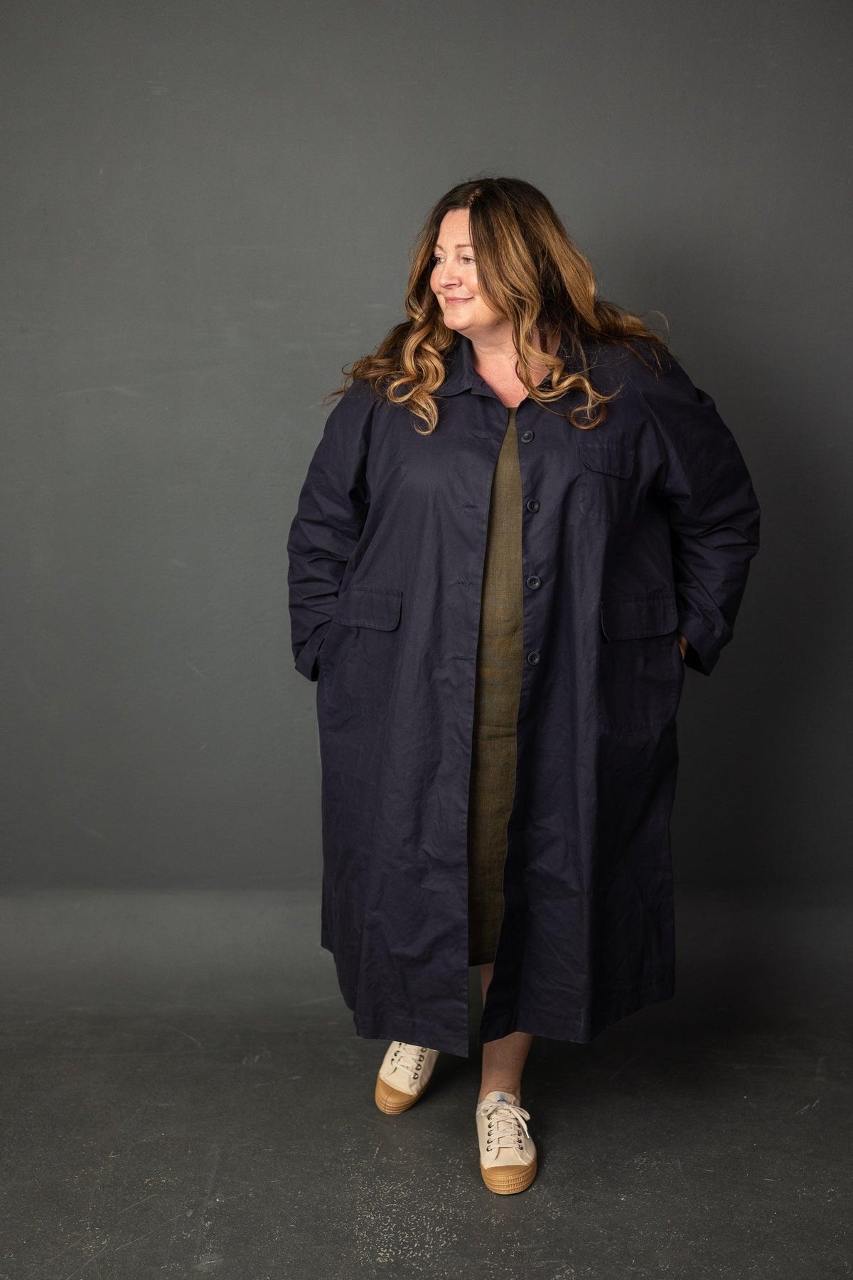 Woman wearing navy button-up coat over olive dress, styled with casual sneakers for everyday wear